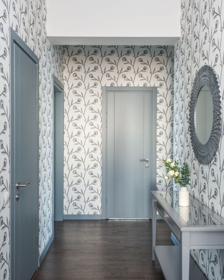 A hallway finished with soft botanical-leaf wallpaper, a round mirror and a slim console table
